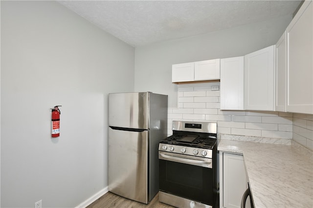 kitchen with appliances with stainless steel finishes, light hardwood / wood-style floors, white cabinetry, decorative backsplash, and a textured ceiling