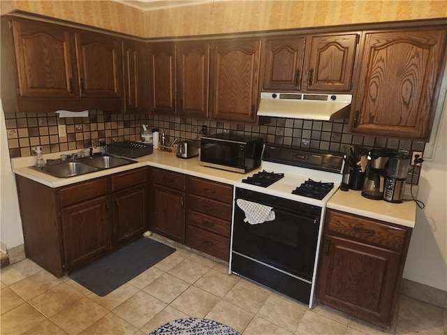 kitchen featuring decorative backsplash, white stove, sink, light tile patterned flooring, and dark brown cabinets