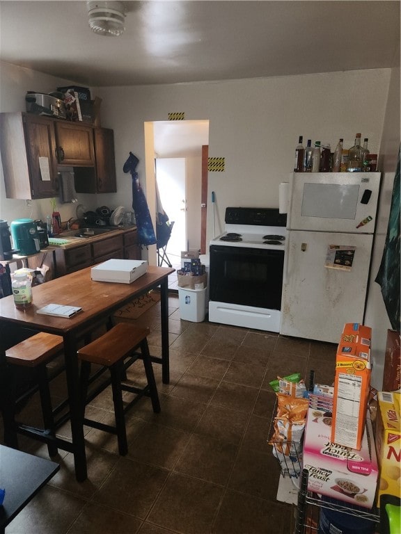 kitchen featuring dark brown cabinets, white appliances, and dark tile patterned flooring