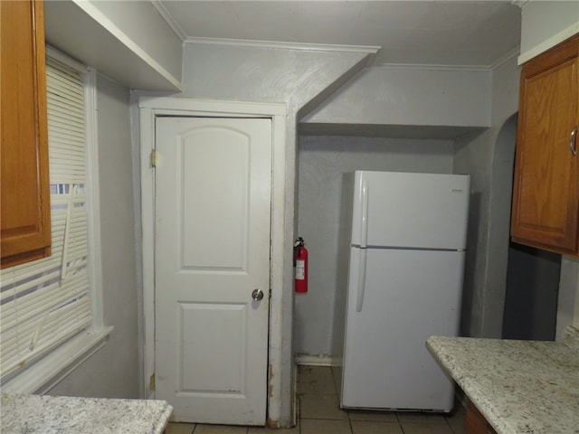 kitchen featuring light stone countertops, white refrigerator, light tile patterned floors, and crown molding