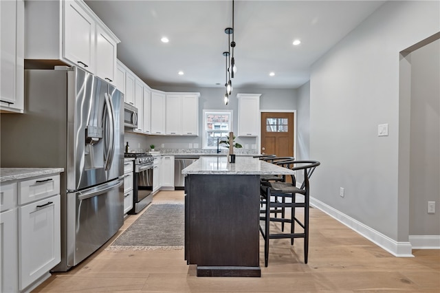 kitchen with appliances with stainless steel finishes, light stone countertops, white cabinetry, and a kitchen island with sink