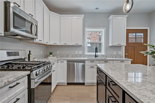 kitchen featuring light stone countertops, light hardwood / wood-style flooring, appliances with stainless steel finishes, sink, and white cabinets