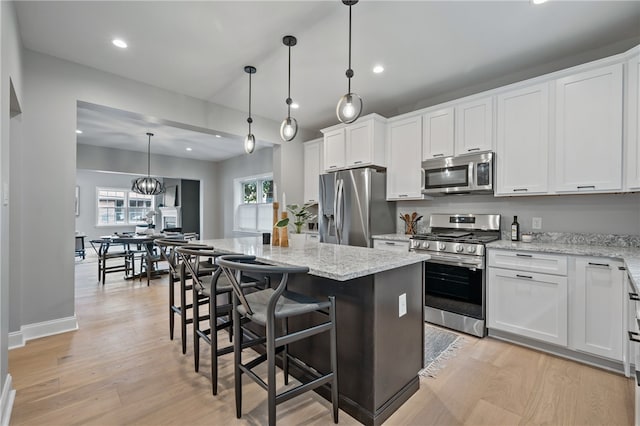 kitchen featuring decorative light fixtures, appliances with stainless steel finishes, a center island, white cabinetry, and light wood-type flooring