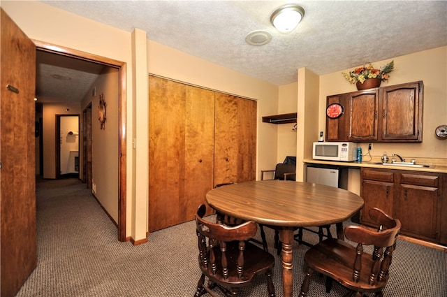 dining space featuring sink, light carpet, and a textured ceiling