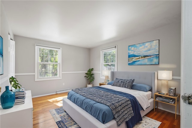 bedroom featuring multiple windows, wood-type flooring, and a baseboard heating unit