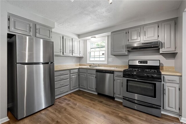 kitchen featuring a textured ceiling, ventilation hood, gray cabinetry, appliances with stainless steel finishes, and dark hardwood / wood-style flooring