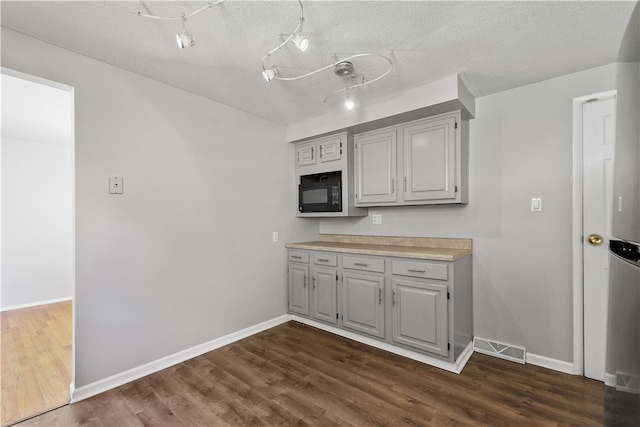 kitchen with a textured ceiling, black microwave, dark wood-type flooring, and gray cabinets