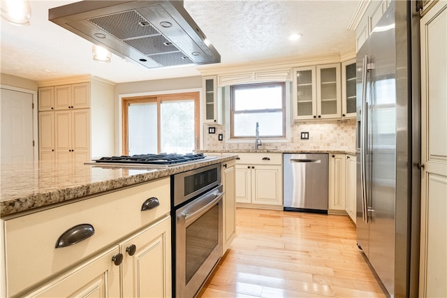 kitchen featuring cream cabinets, light stone counters, extractor fan, light hardwood / wood-style flooring, and stainless steel appliances