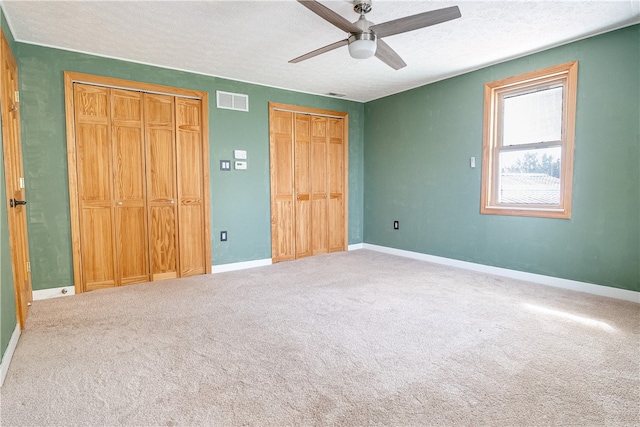 unfurnished bedroom featuring multiple closets, carpet flooring, and ceiling fan