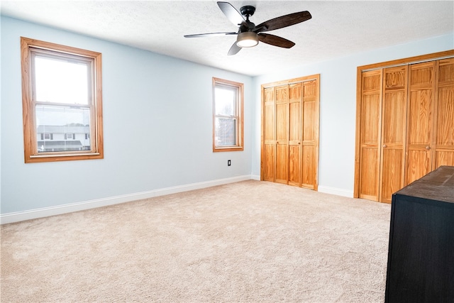 unfurnished bedroom featuring a textured ceiling, two closets, multiple windows, and ceiling fan