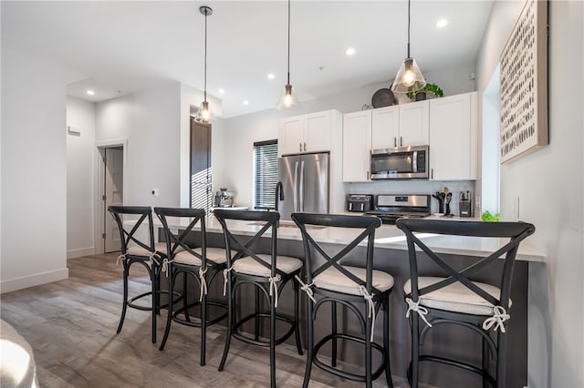 kitchen with decorative light fixtures, appliances with stainless steel finishes, dark hardwood / wood-style floors, and white cabinetry