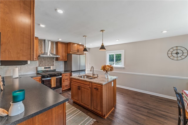 kitchen with pendant lighting, a center island with sink, dark wood-type flooring, wall chimney range hood, and appliances with stainless steel finishes