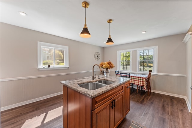 kitchen with hanging light fixtures, sink, a center island with sink, dark hardwood / wood-style floors, and light stone countertops