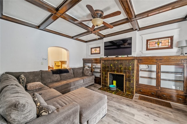 living room with a tiled fireplace, ceiling fan, hardwood / wood-style flooring, beamed ceiling, and coffered ceiling