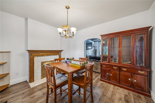 dining room with light hardwood / wood-style floors, an inviting chandelier, and a tiled fireplace