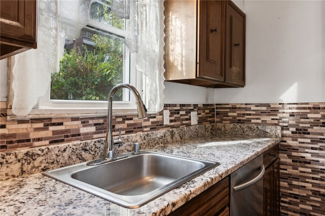 kitchen featuring stainless steel dishwasher, sink, light stone countertops, and dark brown cabinets