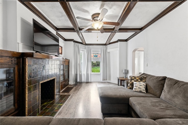 living room featuring hardwood / wood-style floors, ceiling fan, beamed ceiling, a tile fireplace, and coffered ceiling