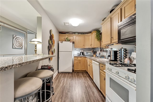 kitchen featuring a breakfast bar, white appliances, light brown cabinets, dark hardwood / wood-style flooring, and light stone countertops