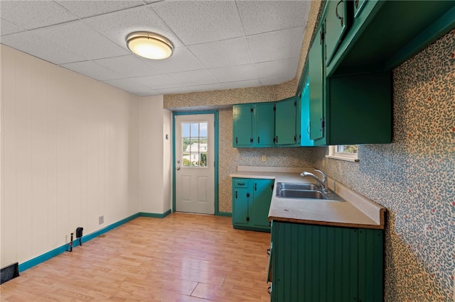 kitchen with wooden walls, light wood-type flooring, a paneled ceiling, and sink