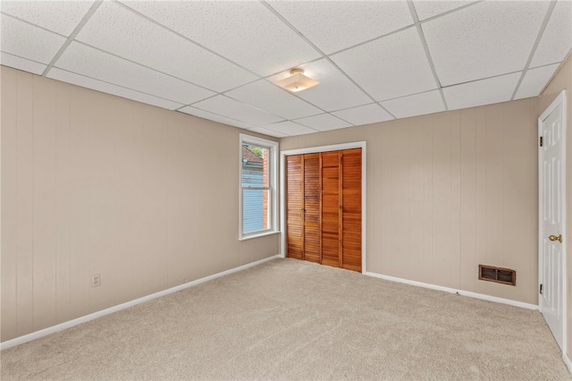 carpeted spare room featuring wooden walls and a paneled ceiling