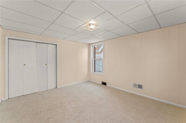 unfurnished bedroom with a drop ceiling, a closet, and light colored carpet