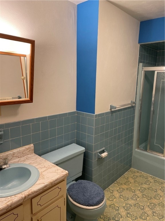 full bathroom featuring tile walls, bath / shower combo with glass door, vanity, and toilet