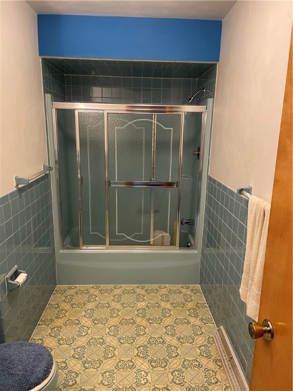 bathroom featuring tile walls, combined bath / shower with glass door, and toilet