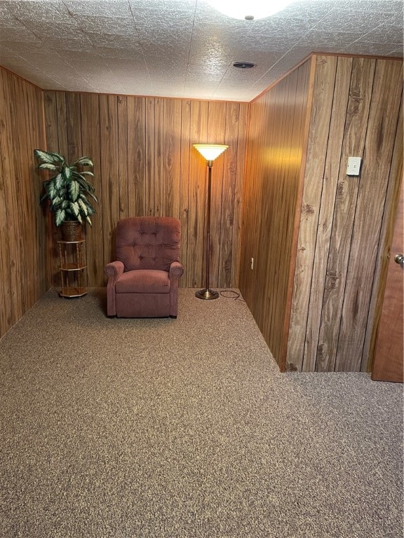 sitting room featuring wood walls, a textured ceiling, and carpet flooring