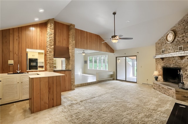 kitchen with ceiling fan, a kitchen island, high vaulted ceiling, light colored carpet, and a fireplace