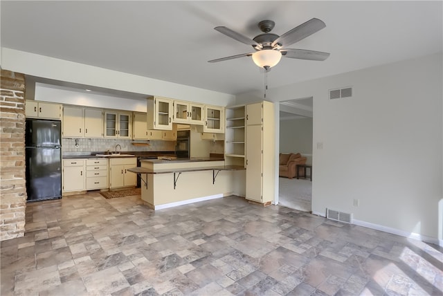 kitchen featuring ceiling fan, tasteful backsplash, cream cabinets, black appliances, and a breakfast bar