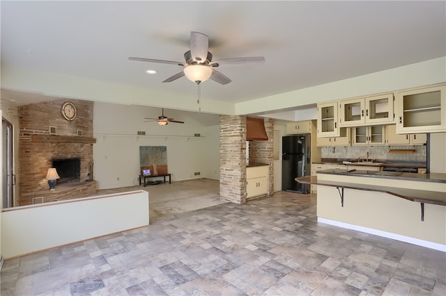 kitchen with ceiling fan, tasteful backsplash, cream cabinetry, a fireplace, and black refrigerator