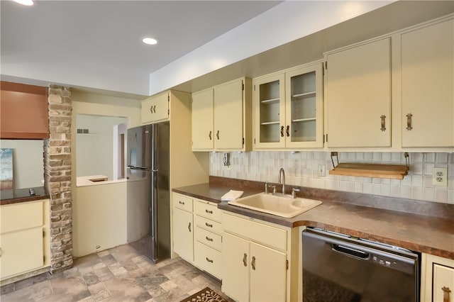 kitchen featuring decorative backsplash, black refrigerator, stainless steel dishwasher, cream cabinets, and sink