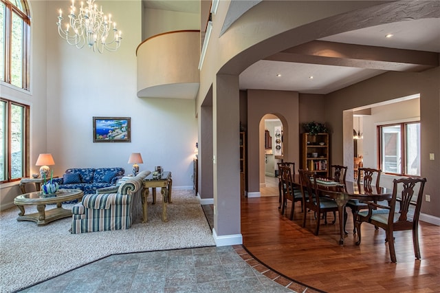 living room featuring wood-type flooring, beamed ceiling, a notable chandelier, and a wealth of natural light