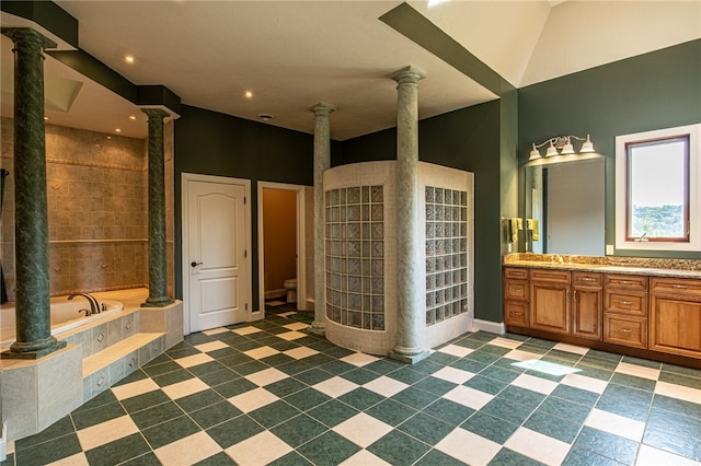 bathroom featuring a relaxing tiled tub, vanity, decorative columns, and toilet