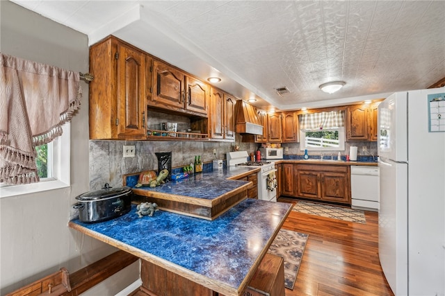 kitchen with kitchen peninsula, a textured ceiling, custom range hood, light hardwood / wood-style floors, and white appliances