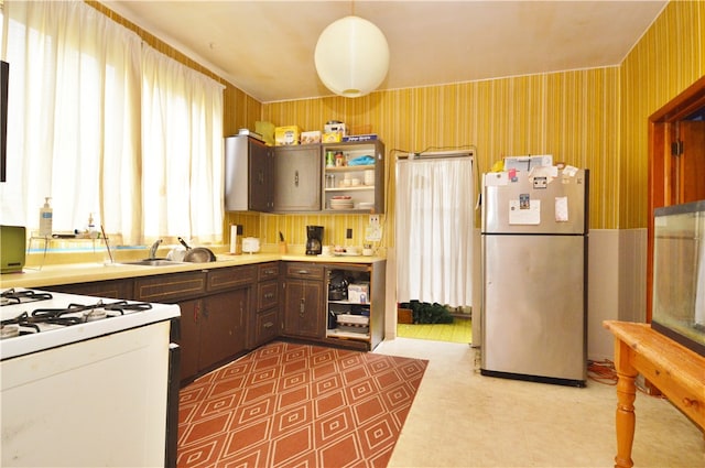 kitchen with white range with gas stovetop, stainless steel refrigerator, dark brown cabinetry, and sink