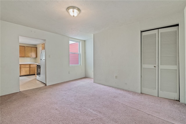 unfurnished bedroom featuring a closet, connected bathroom, white refrigerator, light colored carpet, and a textured ceiling