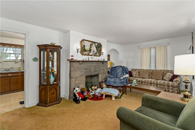 carpeted living room with sink and a stone fireplace