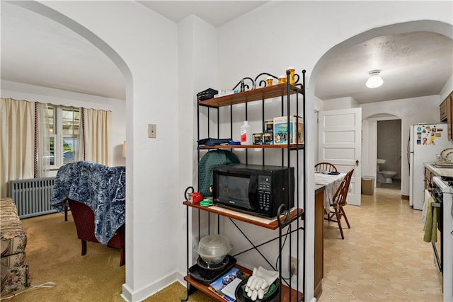 kitchen with radiator heating unit, white appliances, and light carpet