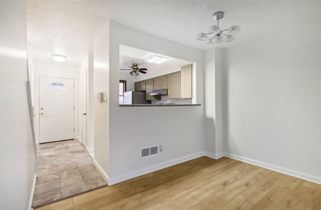 unfurnished living room featuring ceiling fan with notable chandelier and light hardwood / wood-style flooring