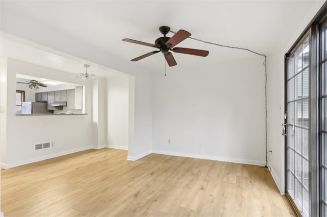 unfurnished room featuring ceiling fan with notable chandelier and light hardwood / wood-style flooring