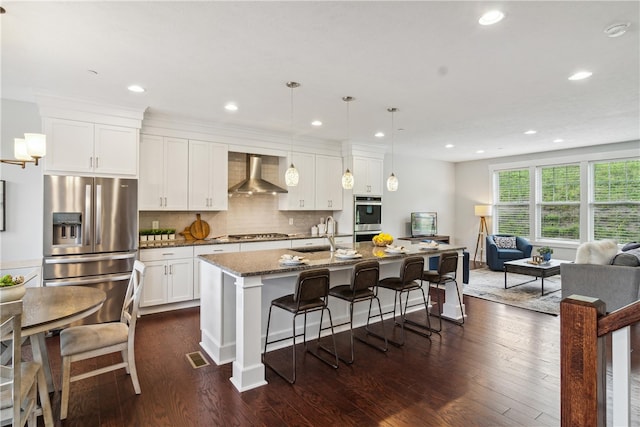 kitchen featuring sink, wall chimney exhaust hood, stainless steel appliances, dark stone countertops, and a center island with sink