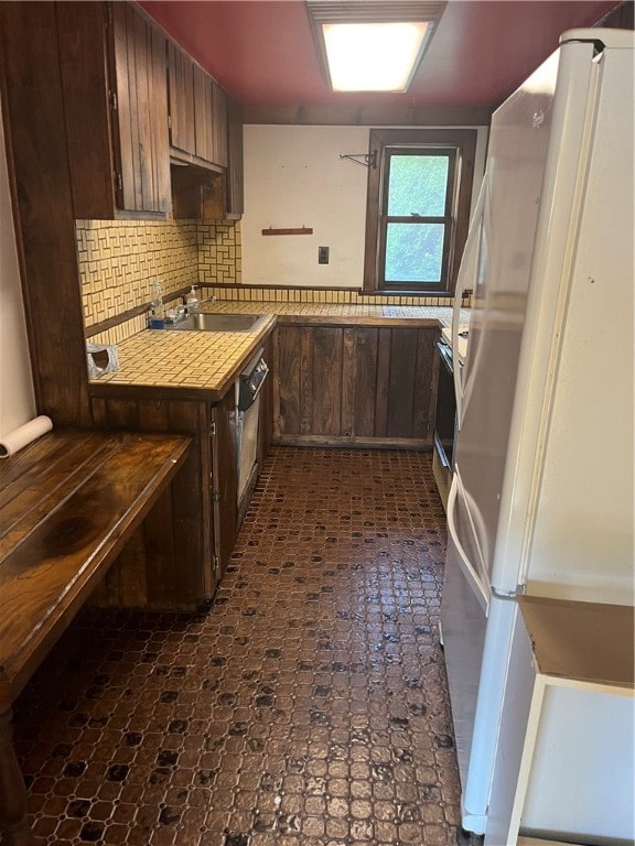 kitchen with dark brown cabinetry, white refrigerator, and decorative backsplash