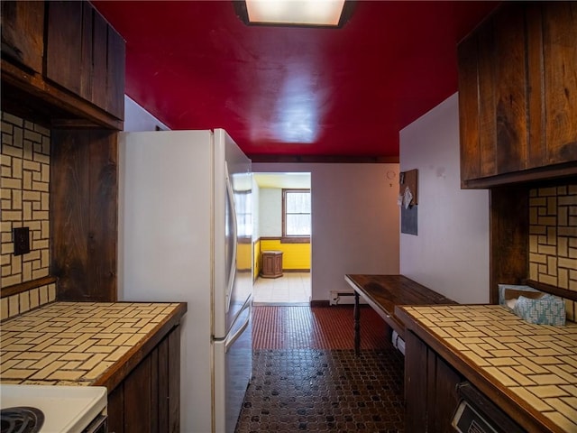 kitchen featuring white refrigerator, dark brown cabinets, tile countertops, and decorative backsplash