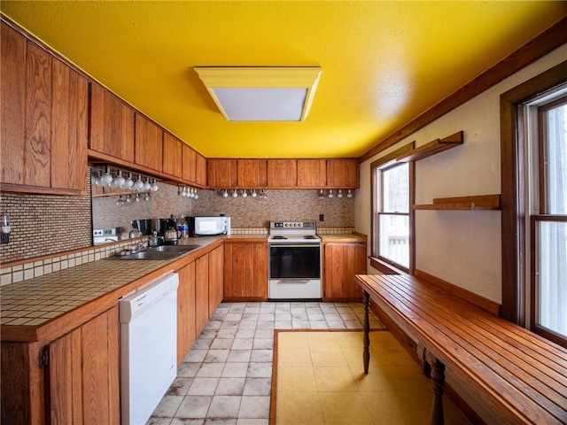 kitchen with sink, white appliances, tasteful backsplash, light tile patterned flooring, and tile countertops