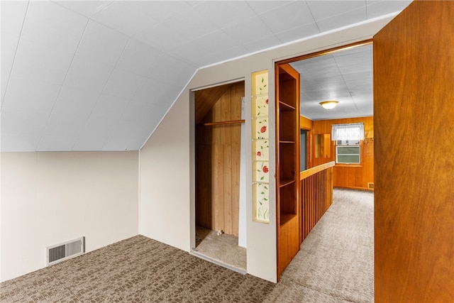 additional living space with light carpet, wooden walls, and vaulted ceiling