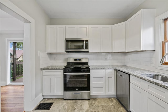 kitchen featuring decorative backsplash, appliances with stainless steel finishes, sink, white cabinets, and light hardwood / wood-style floors