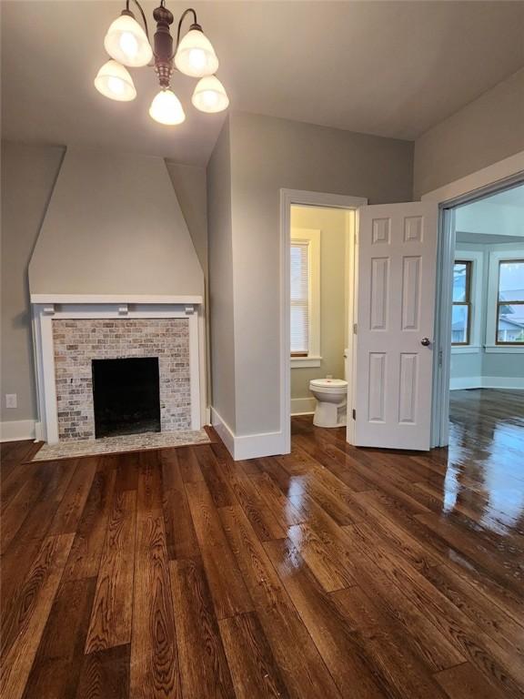 unfurnished living room with a wealth of natural light, a chandelier, dark hardwood / wood-style floors, and a brick fireplace