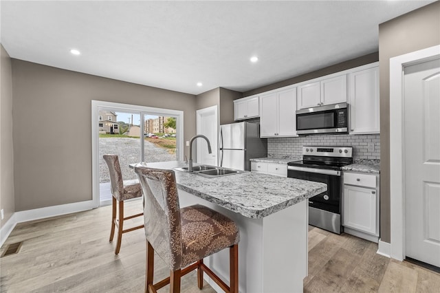 kitchen with white cabinets, a kitchen island with sink, stainless steel appliances, a breakfast bar area, and light wood-type flooring