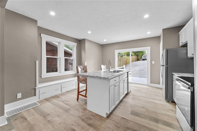 kitchen with light wood-type flooring, a center island with sink, white cabinetry, and stainless steel electric range oven